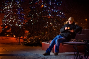 A young man sits on a bench and drink coffee at Christmas, snowfall